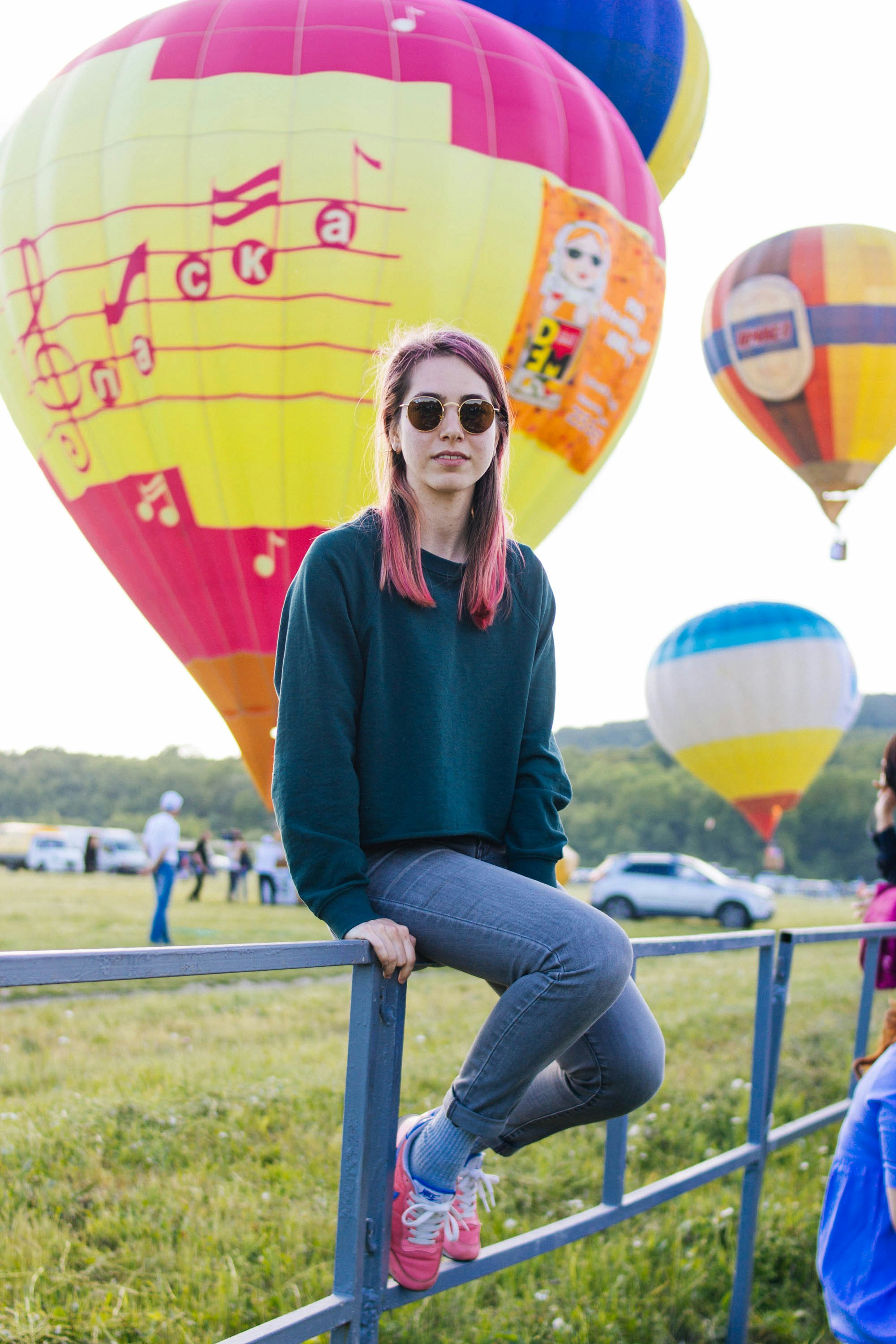 woman in green sweater and blue denim jeans sitting on green grass field with hot air